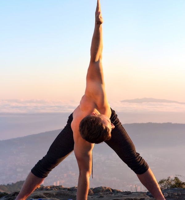 Person stretching arms towards the sky during a sunrise yoga session on a mountain.